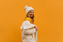 Beautiful Curly Blonde In Orange Sweater Puts On Eco Fur Coat And Looks Down Flirty