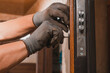 Close-up, the carpenter installs a custom lock in the front metal door, using a drill and hammer and other tools.
