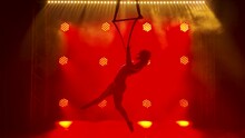 Flexible Pretty Brunette Woman In A Purple Tight Fitting Suit Performs Acrobatic Elements In An Air Hoop. A Spinning Circus Performer Silhouetted Against A Background Of Red Neon Lights. Slow Motion.