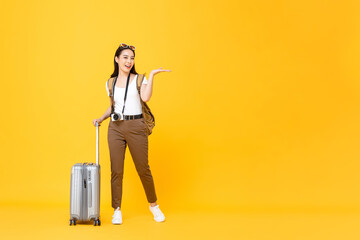 Full length portrait of smiling cute young Asian woman tourist open hand to copy space isolated on yellow studio background