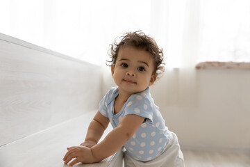 portrait of adorable little african american baby boy or girl relying on furniture, learning making 