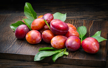 Ripe juicy plums with leaves on a wooden background.