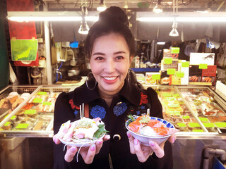 Tourist woman showing salmon sashimi most popular delicious food in street food tsukiji fish market, Japan