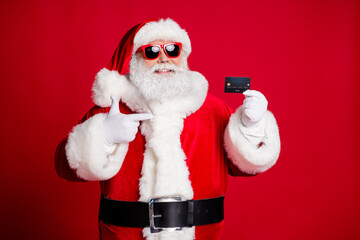 Portrait of his he nice handsome cheerful bearded Santa holding in hand demonstrating card shop cash pay payment presentation isolated bright vivid shine vibrant red color background