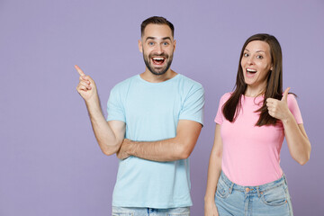 Excited cheerful young couple two friends man woman in blue pink t-shirts showing thumb up pointing index finger aside up on mock up copy space isolated on violet colour background studio portrait.