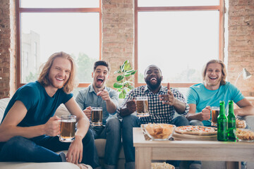 Portrait of crazy four people buddies sit comfort couch watch joke comedy series hold beer pint mug point finger laughing have crisps chips in house indoors