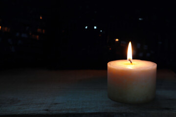 aromatic scented ivory colour pillar candle is lighting on the wooden table in the dark garden at night in the winter