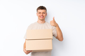 Wall Mural - Young handsome man over isolated white background holding a box to move it to another site with thumb up