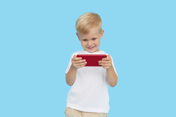 Cute smilling child boy with smartphone on blue background. Advertising of educational applications on a mobile phone for children. Funny face.