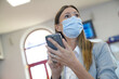 Businesswoman waiting at train station, wearing face mask and using smartphone