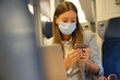 Businesswoman commuting by train, working on laptop and wearing face mask