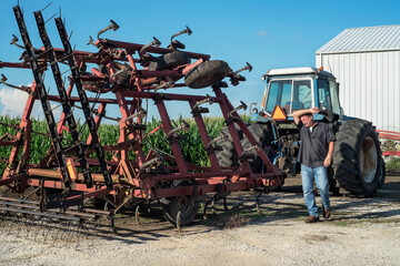 Farmer wiping sweat from his forehead on hot, summer day on farm, equipment, tractor and corn field in background, agriculture, agricultural, farming, hard work, worker, occupation 