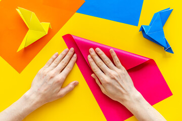 Wall Mural - Female hands folding sheet of paper - origami bird. Overhead view