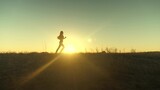 Fototapeta Kosmos - running after sun. training jogging. healthy beautiful girl is engaged in fitness, jogging in country in sun. Jogger girl breathes fresh air on field. Free young woman runs in summer park at sunset.