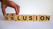 Hand turns a cube and changes the word delusion to illusion. Beautiful white background. Business concept. Copy space.