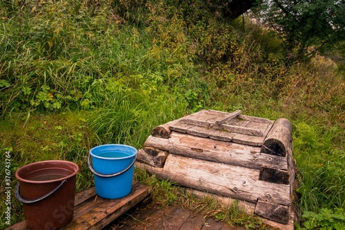 Fotomural Rural retro landscape with wooden well and buckets of water on a hillside with g
