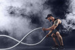 © zamuruev - Bearded athletic looking bodybulder work out with battle rope on dark studio background with smoke. Strength and motivation.