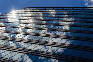 The blue sky with clouds is reflected in the glass of identical windows of modern office building