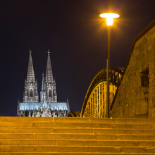 Stairway With View Of Hohenzollern Bridge (Hohenzollernbruecke) And Cologne Cathedral (Koelner Dom) Spires At Night, Cologne, Germany
