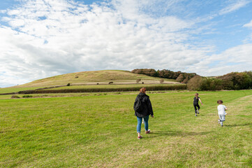 Family day out in the countryside with a green lush grass, fields and meadows against blue cloudy sky.