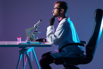 Poster - the chemist paused at the microscope. the chemist is sitting in a chair, sideways to the camera. lab