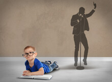 Little Boy With Book Dreaming To Be Singer. Silhouette Of Man Behind Kid's Back