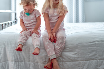 two little girls sitting on the edge of the bed in their pajamas