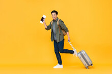 Full Length Portrait Of Smiling Happy Handsome Young Asian Man Tourist With Passport And Luggage Ready To Travel On Vacations Isolated In Yellow Studio Background