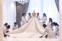 Team Of Female Dressmaking Workers Preparing A Large Haute Couture Wedding Dress On A Mannequin In A Bridal Design Studio.