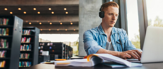 Male student working on laptop at public library