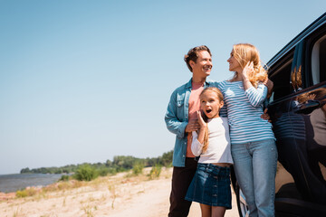 Wall Mural - Selective focus of man embracing wife near shocked daughter and car on beach