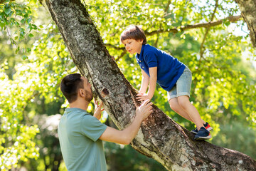 Canvas Print - family, fatherhood and people concept - happy father with little son climbing tree in summer park