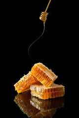 Sweet honeycomb and golden dipper with dripping honey on black background with reflection, bee products by organic natural food ingredients. Beekeeping advertisement, banner