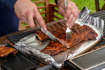 Gourmet BBQ on a table. The Man hands cutting freshly prepared barbecue pork ribs. Dinner party at homes terrace.