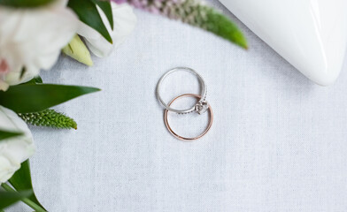 Wedding ring and diamond ring on a white background with flowers and a white shoe of the bride. View from above