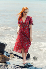 Redhead woman in dress enjoys a walking near the sea shore.