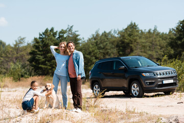 Wall Mural - Selective focus of man hugging wife near daughter with golden retriever during vacation