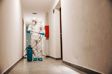 Wall Mural - Full length of man in sterile suit disinfecting hall of the building. Protection from corona concept.