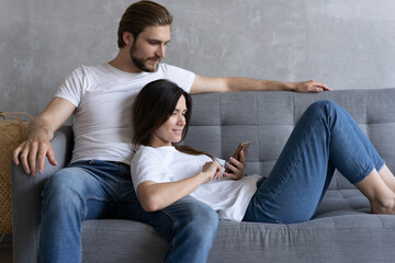 Wall Mural - Happy couple enjoying media content in a smart phone sitting on a couch at home