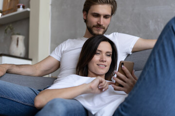 Wall Mural - Happy couple enjoying media content in a smart phone sitting on a couch at home