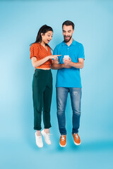 Wall Mural - excited asian woman pointing with finger at smartphone in hands of bearded man while levitating on blue