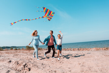 Wall Mural - Selective focus of kid holding kite while running on beach near parents