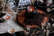 Spell Casting On Samhain (Halloween) To Contact Spirits Of Dead Relatives. Dark And Mysterious Wiccan Witch Altar Filled With Vintage Postcards, Photos, Memorabilia, Burning Candles, Dirt, Black Earth