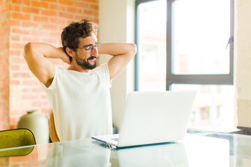 Wall Mural - young bearded man with a laptop smiling and feeling relaxed, satisfied and carefree, laughing positively and chilling