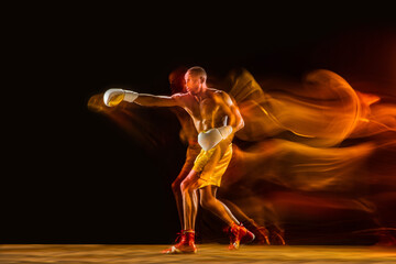 Fireball. Professional boxer training isolated on black studio background in mixed light. Man in gloves practicing in kicking and punching. Healthy lifestyle, sport, workout, motion and action concept