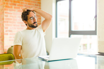 Wall Mural - young bearded man with a laptop smiling cheerfully and casually, taking hand to head with a positive, happy and confident look