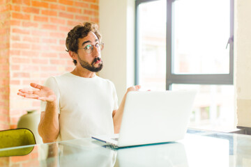 Wall Mural - young bearded man with a laptop feeling puzzled and confused, unsure about the correct answer or decision, trying to make a choice