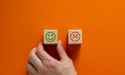 Close up customer hand choose smiley face icon on wood cube. Service rating, satisfaction concept. Copy space, beautiful orange background.