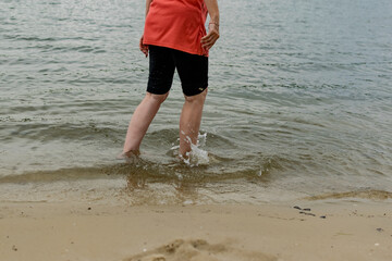 Women's feet barefoot in the water on the sandy wet shore. Summer, freshwater beach. Walk along the river Bank, legs close-up.