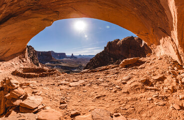 view of a valley from under an arch made of red rock by natural erosion 